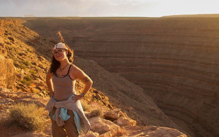 A person smiles as they pose for a photo on top of a canyon